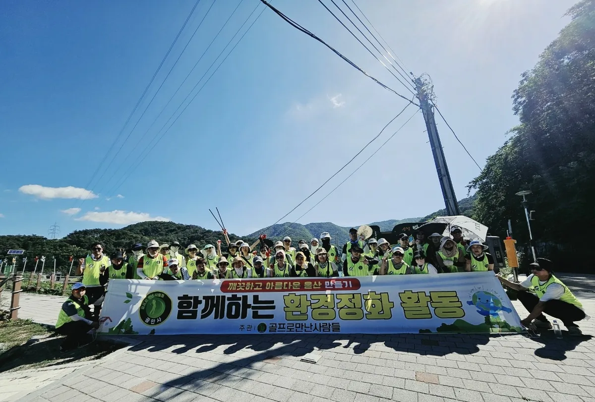 여름 산자락 광장에서 형광 조끼를 입고 환경정화 현수막 뒤에 모여 선 회원들